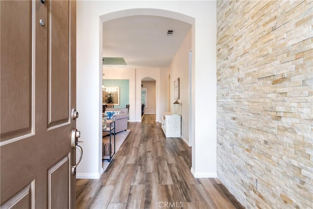 hallway featuring arched walkways, visible vents, baseboards, and wood finished floors