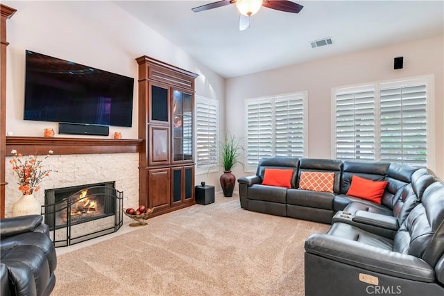 living room with lofted ceiling, visible vents, a ceiling fan, light carpet, and a stone fireplace