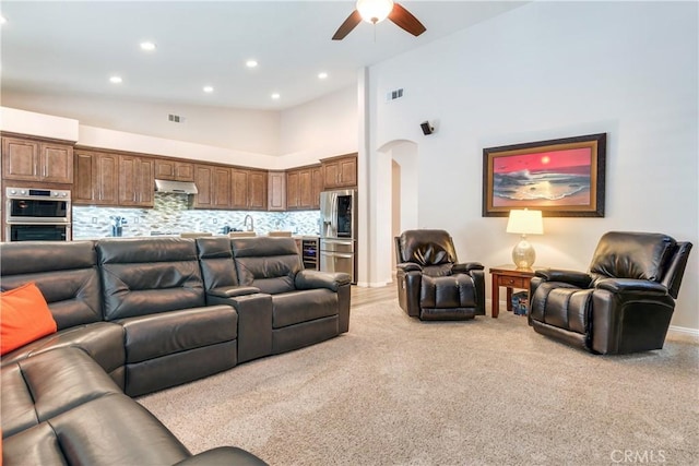 living area featuring arched walkways, high vaulted ceiling, visible vents, and light colored carpet