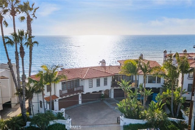 exterior space with a chimney, stucco siding, a water view, driveway, and a tiled roof