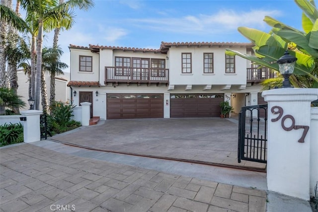 mediterranean / spanish-style house with stucco siding, concrete driveway, an attached garage, a gate, and a balcony