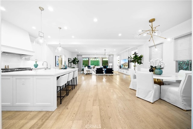 kitchen with decorative light fixtures, an inviting chandelier, light hardwood / wood-style floors, premium range hood, and white cabinets