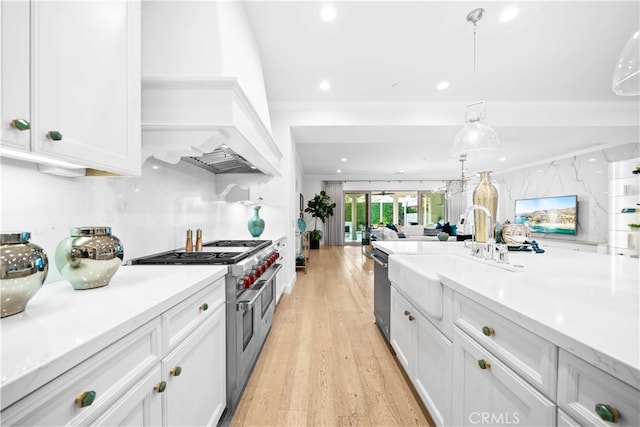 kitchen with appliances with stainless steel finishes, sink, light hardwood / wood-style floors, white cabinets, and hanging light fixtures