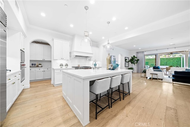 kitchen with a center island with sink, hanging light fixtures, light hardwood / wood-style flooring, white cabinets, and crown molding