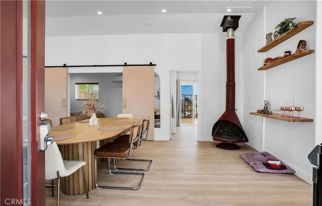 dining room with a barn door, a wall mounted AC, light hardwood / wood-style floors, and a wood stove