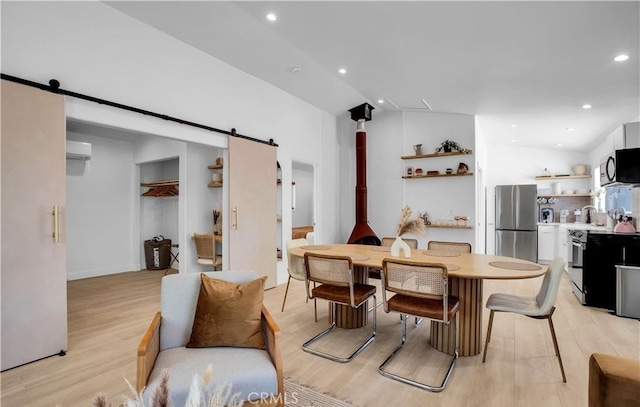 dining room with vaulted ceiling, a barn door, light hardwood / wood-style floors, and a wall unit AC