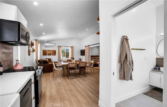 kitchen featuring electric range oven, white cabinetry, lofted ceiling, a barn door, and a wall unit AC