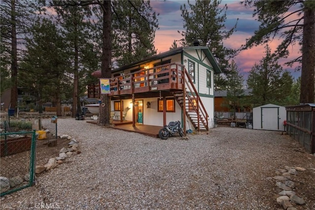 back house at dusk with a wooden deck and a storage unit