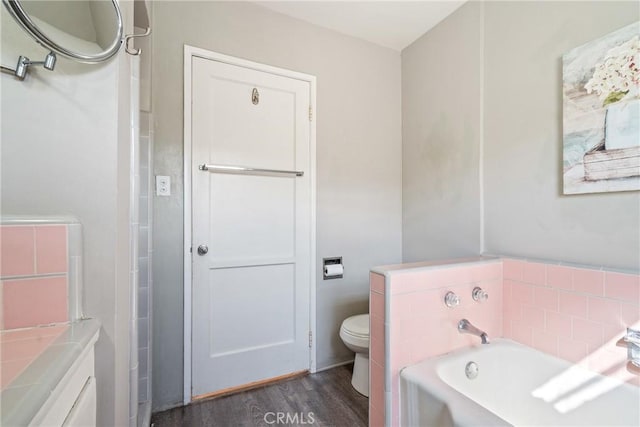 bathroom with a garden tub, toilet, and wood finished floors