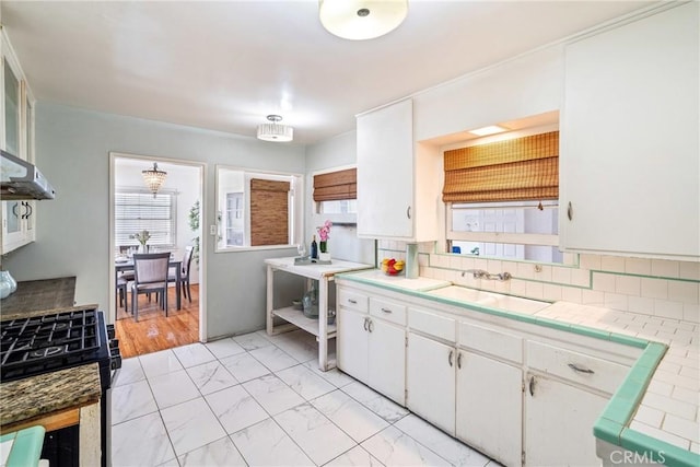 kitchen featuring marble finish floor, tile countertops, gas range oven, white cabinets, and a sink