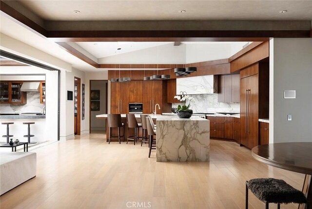 kitchen with modern cabinets, a breakfast bar area, wall chimney range hood, vaulted ceiling, and brown cabinetry