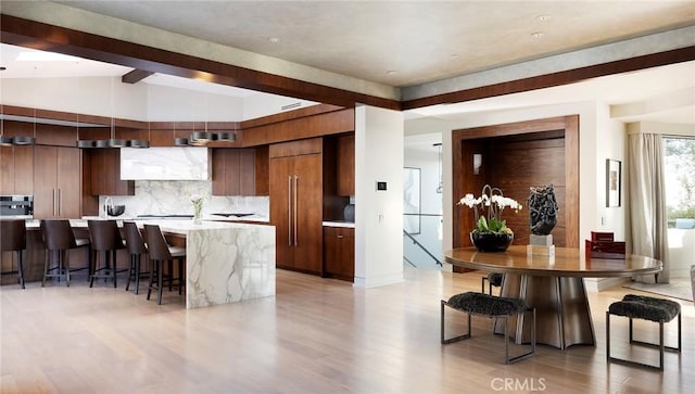 kitchen featuring a kitchen bar, lofted ceiling with beams, a large island, light hardwood / wood-style floors, and backsplash