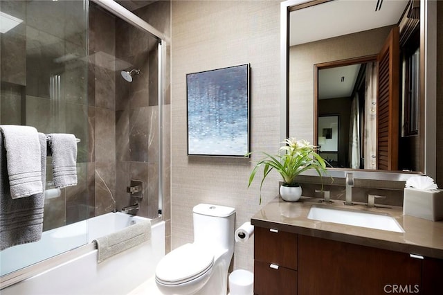 full bathroom featuring bath / shower combo with glass door, tile walls, vanity, and toilet