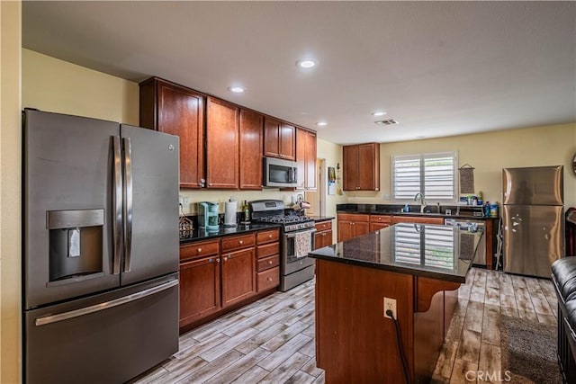 kitchen featuring visible vents, a kitchen island, stainless steel appliances, wood finish floors, and a sink