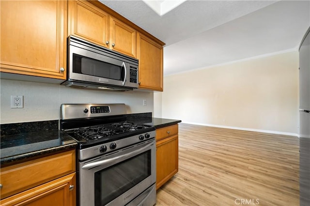 kitchen featuring dark stone countertops, crown molding, light wood-type flooring, and appliances with stainless steel finishes