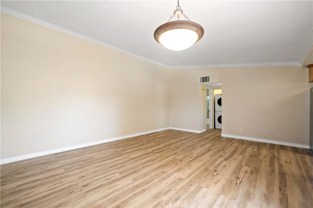 unfurnished room with stacked washing maching and dryer, crown molding, and light hardwood / wood-style flooring