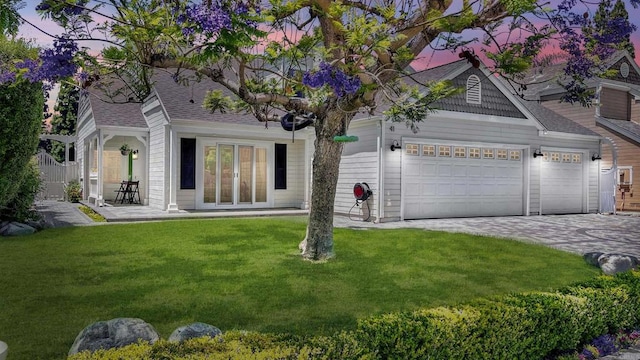 view of front facade featuring a shingled roof, an attached garage, decorative driveway, french doors, and a front lawn