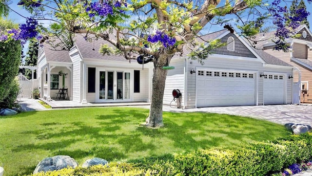 view of front of home featuring a front lawn, decorative driveway, french doors, an attached garage, and a shingled roof