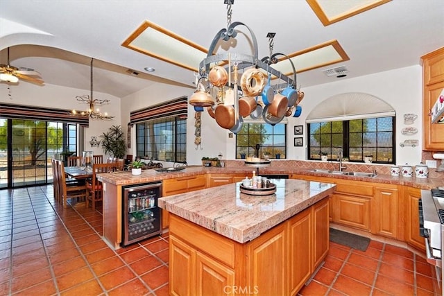 kitchen with a kitchen island, ceiling fan with notable chandelier, sink, beverage cooler, and hanging light fixtures