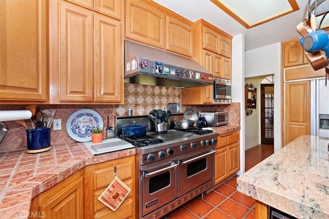 kitchen with light tile patterned flooring, stainless steel appliances, range hood, and decorative backsplash