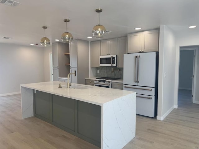 kitchen with hanging light fixtures, gray cabinetry, light stone counters, premium appliances, and sink