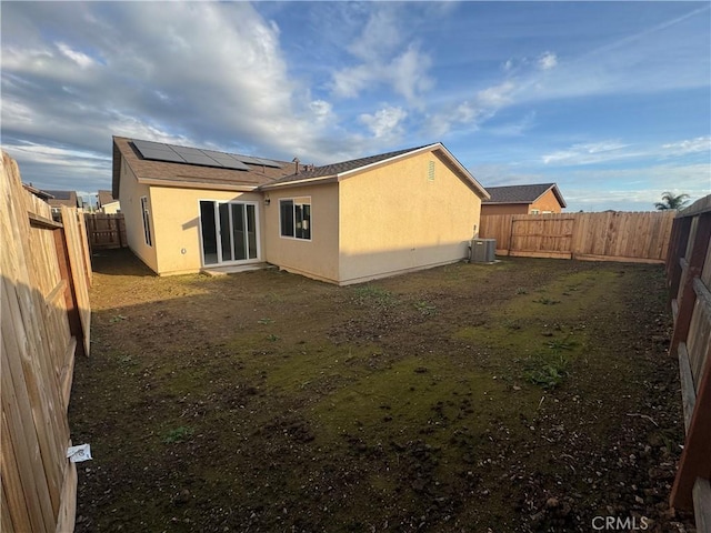 back of house with solar panels, stucco siding, a fenced backyard, and central air condition unit