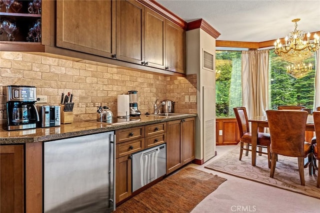 kitchen featuring sink, an inviting chandelier, stainless steel refrigerator, pendant lighting, and backsplash