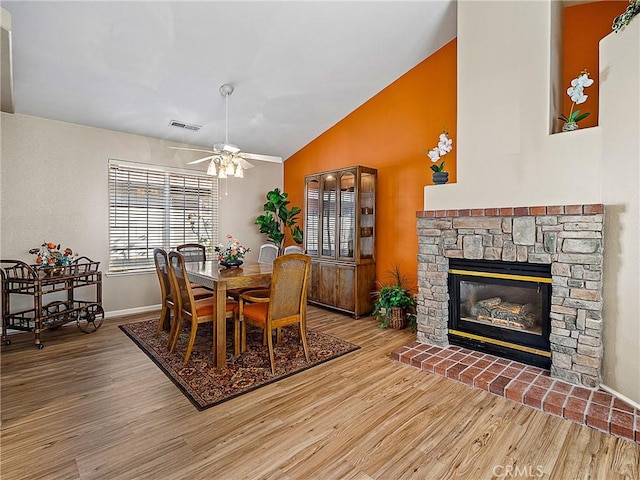 dining area with visible vents, a ceiling fan, wood finished floors, a fireplace, and vaulted ceiling