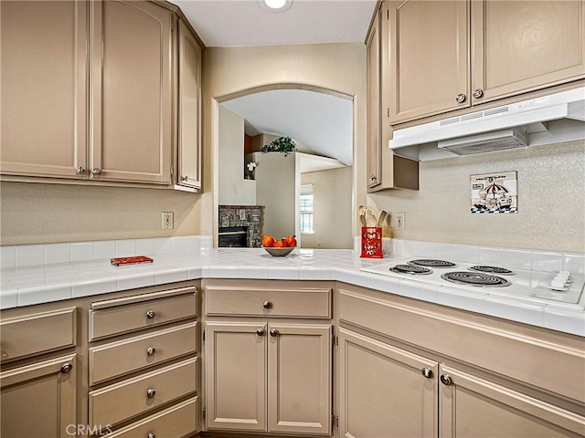 kitchen with under cabinet range hood, arched walkways, white electric cooktop, and a stone fireplace