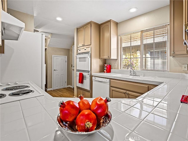 kitchen featuring white appliances, tile countertops, recessed lighting, a sink, and extractor fan