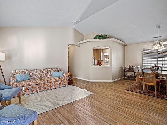 living area featuring visible vents, baseboards, vaulted ceiling, wood finished floors, and arched walkways