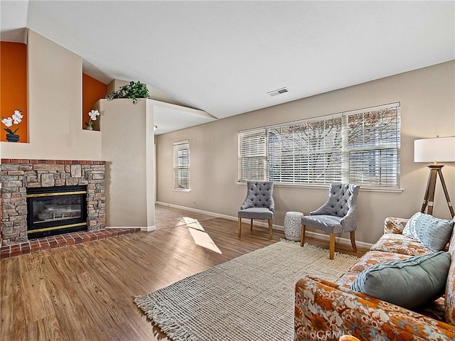 living area featuring wood finished floors, visible vents, baseboards, lofted ceiling, and a fireplace