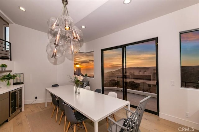 dining area with light wood-type flooring, baseboards, a notable chandelier, wine cooler, and recessed lighting