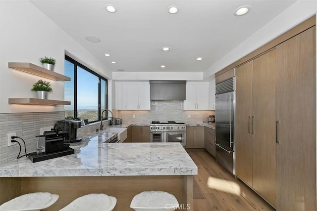 kitchen with kitchen peninsula, sink, custom range hood, white cabinets, and premium appliances