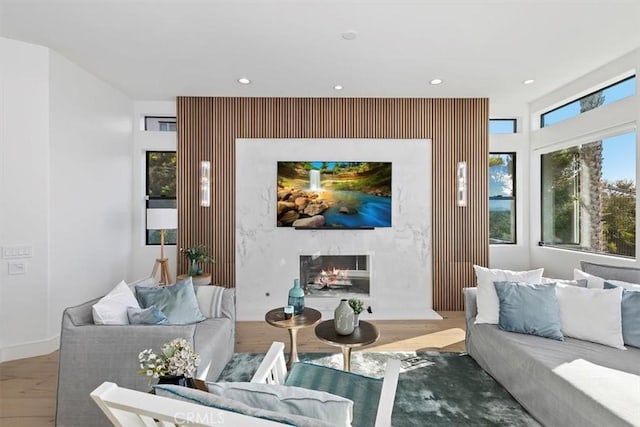 living area with an accent wall, recessed lighting, wood finished floors, and a premium fireplace