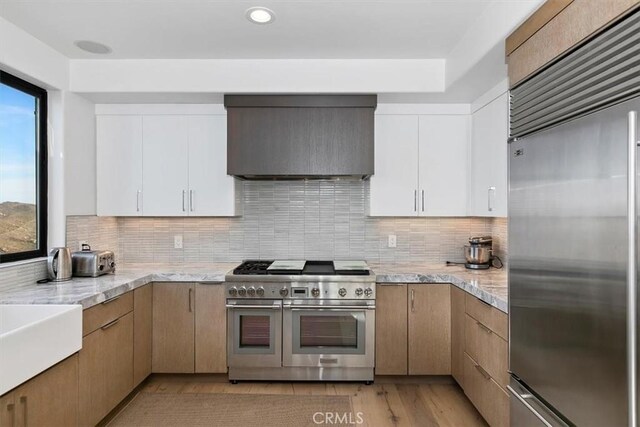 kitchen with decorative backsplash, high quality appliances, light wood-type flooring, white cabinets, and custom range hood