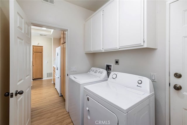 washroom with washing machine and dryer, cabinets, and light hardwood / wood-style floors
