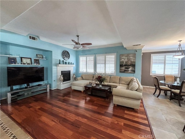 living area featuring crown molding, a tile fireplace, a ceiling fan, and visible vents