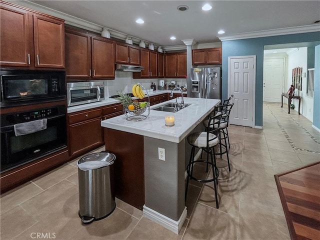kitchen featuring crown molding, black appliances, under cabinet range hood, a breakfast bar area, and a sink