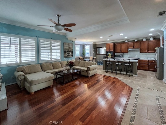 living area with visible vents, ornamental molding, and ceiling fan
