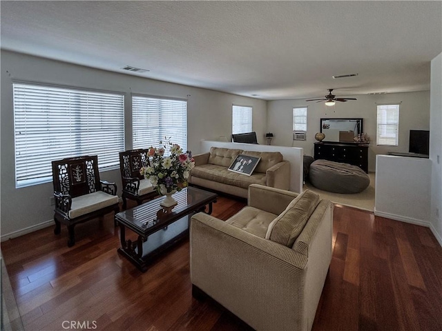 living area with dark wood-style flooring, visible vents, baseboards, and a ceiling fan