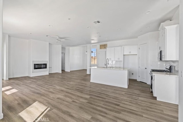 kitchen with sink, hardwood / wood-style flooring, a kitchen island with sink, white cabinetry, and stainless steel appliances