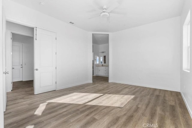 unfurnished bedroom featuring ceiling fan, ensuite bath, and wood-type flooring