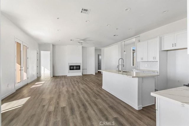 kitchen featuring sink, a kitchen island with sink, light stone countertops, white cabinets, and dark hardwood / wood-style flooring