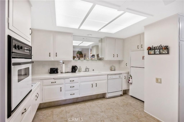 kitchen featuring white appliances, a sink, white cabinetry, and decorative backsplash