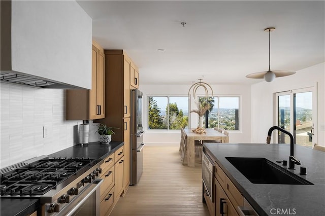 kitchen featuring stainless steel range with gas stovetop, a sink, decorative backsplash, dark countertops, and wall chimney range hood