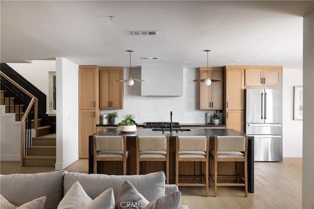 kitchen with light wood-type flooring, freestanding refrigerator, a sink, a kitchen breakfast bar, and tasteful backsplash