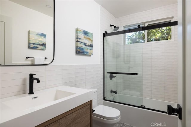 full bath with toilet, tile walls, vanity, and shower / bath combination with glass door