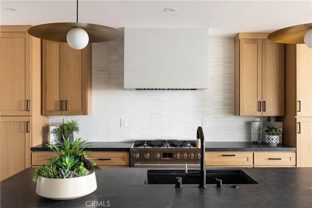 kitchen with ventilation hood, stainless steel range with gas stovetop, decorative backsplash, hanging light fixtures, and a sink