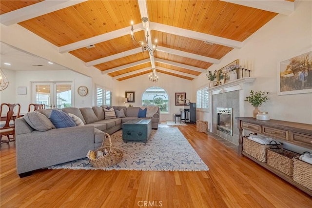 living room featuring a tiled fireplace, wood ceiling, light hardwood / wood-style flooring, a notable chandelier, and lofted ceiling with beams